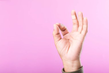 İndeks ve orta parmaklarda yara bandı olan bir el, küçük aksiliklere rağmen devam etmek için güç ve kararlılığı sembolize eden bir 'Tamam' işareti yapıyor.