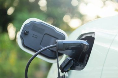 Bir elektrikli araç şarj aleti şarj portuna takılır, temiz ve yeşil enerjiye geçişi sembolize eder. Sürdürülebilir teknoloji ve çevre dostu uygulamalara odaklanıldı