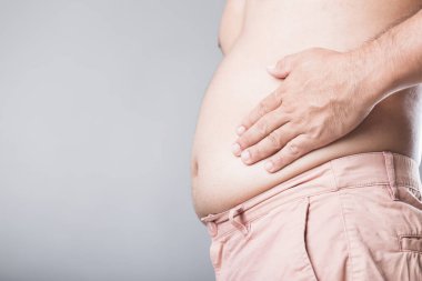 Bir adam elini sol karnına bastırıyor ve aşırı kilolardan kaynaklanan böbrek sorunlarıyla bağlantılı olma ihtimali var. Görüntü, erkek sağlığını ve obezitenin iç organlar üzerindeki etkisini vurguluyor