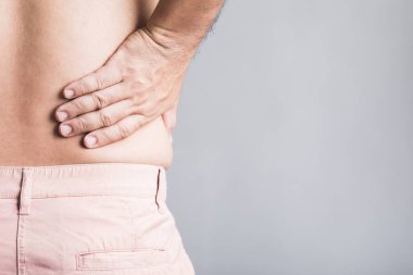 Bir adam elini beline bastırıyor, belindeki ve kalçasındaki kas ağrısından rahatsızlık duyuyor, muhtemelen aşırı kilolardan kaynaklanıyor. Obezitenin kas iskeleti sağlığı üzerindeki etkileri