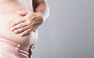 Bir adam elini sol karnına bastırıyor ve aşırı kilolardan kaynaklanan böbrek sorunlarıyla bağlantılı olma ihtimali var. Görüntü, erkek sağlığını ve obezitenin iç organlar üzerindeki etkisini vurguluyor
