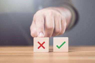 Tahta bloklardaki işaretle X işareti arasında seçim yapan bir adam. Resim, doğru ve yanlış arasındaki farkı vurgulayarak doğru seçimi yapma kavramını temsil eder.