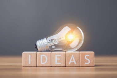 A light bulb next to wooden letters spelling 'IDEAS' arranged on a table symbolizes the spark of new ideas and creativity. This image reflects inspiration and the pursuit of innovative thinking clipart