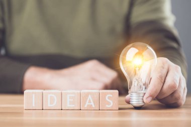 Masaya yerleştirilmiş 'IDEAS' harflerinin yanındaki ampul yeni fikirlerin ve yaratıcılığın kıvılcımını sembolize ediyor. Bu görüntü ilham ve yenilikçi düşünce arayışını yansıtır.