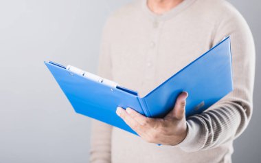 Adamın biri mavi bir hayat sigortası poliçesi tutuyor. Detayları gri arka planda okuyup gözden geçiriyor. Bu resim finansal güvenliği anlamanın ve planlamanın önemini vurgular.