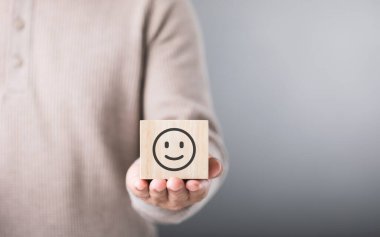 Adam gülen bir yüzle ahşap bir blok tutuyor, pozitifliği ve mutluluğu sembolize ediyor. Bu görüntü neşeyi kucaklama ve iyimser bir görünümü sürdürme kavramını yansıtır.