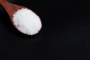 Tahta kaşıkta yakın plan beyaz şeker. Karanlık ve karamsar arkaplan.