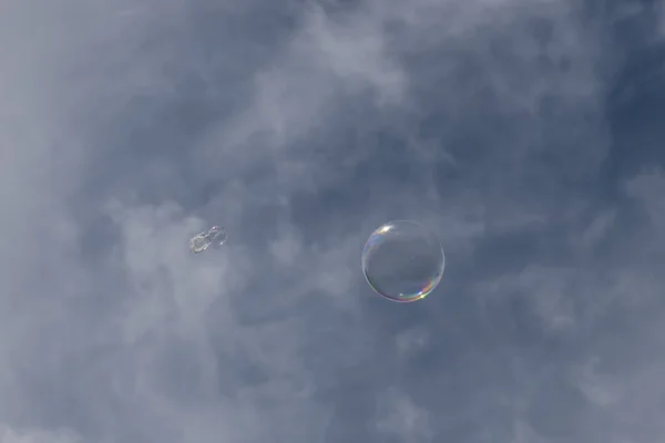 A clear bubble with reflection against a blue sky with white clouds.