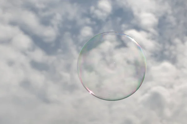 A clear bubble with reflection against a blue sky with white clouds.