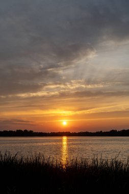 ABD 'nin Minnesota kentindeki Kuzey Kaplumbağa Gölü' nde bulutlarla, Tanrı 'nın ışınlarıyla ve ağaçlarla portakal rengi yaz günbatımı