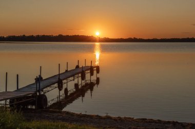Minnesota, ABD 'deki Ten Mile Gölü' nde bir rıhtım ve yansımasıyla turuncu yaz günbatımı.