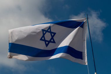 Güneşli bir günde beyaz bulutlu mavi gökyüzüne karşı İsrail bayrağı.