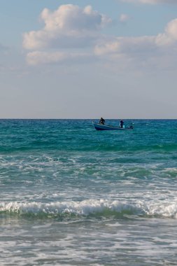 Two fishermen in their boat looking for a good place to catch some fish in the Mediterranean Sea near HaBonim Beach in Israel. clipart