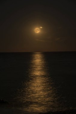 Gece, ay alışılmadık bir renkle parlar, denizin yüzeyinde bir ay yolu bırakır, Liguria, İtalya