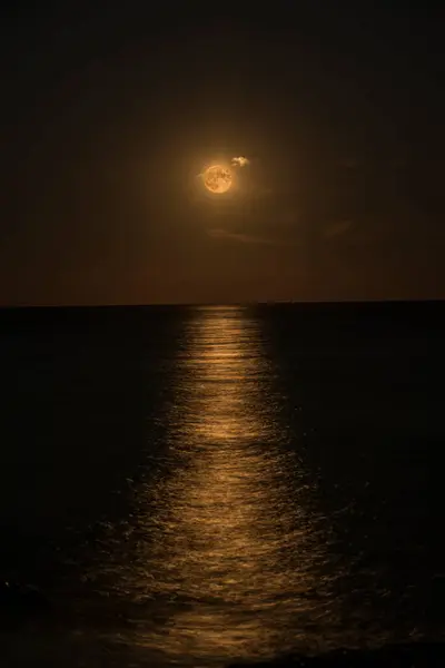 Gece, ay alışılmadık bir renkle parlar, denizin yüzeyinde bir ay yolu bırakır, Liguria, İtalya