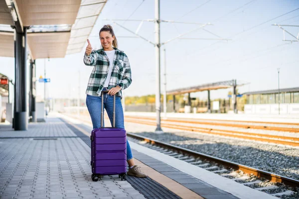 幸せな女性とともにスーツケース立って電車の駅と上に親指を表示 — ストック写真