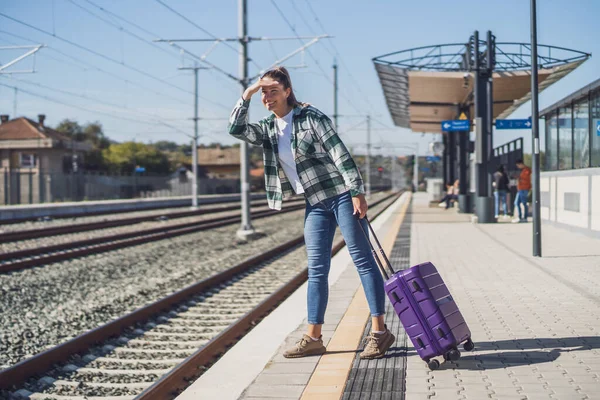 鉄道駅で列車を待っている間 幸せな女性は離れて見ている — ストック写真