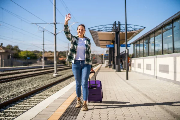 スーツケースを持った幸せな女性が駅を歩いて手を振る — ストック写真