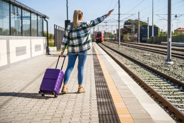提着手提箱向车站的火车挥手的女人 — 图库照片