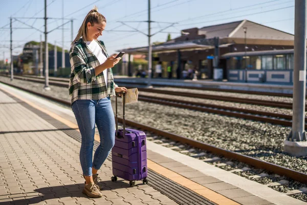 Szczęśliwa Kobieta Pomocą Telefonu Komórkowego Trzymając Mapę Stacji Kolejowej — Zdjęcie stockowe