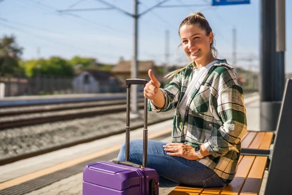 Szczęśliwa Kobieta Pokazuje Kciuk Górę Siedząc Ławce Stacji Kolejowej — Zdjęcie stockowe