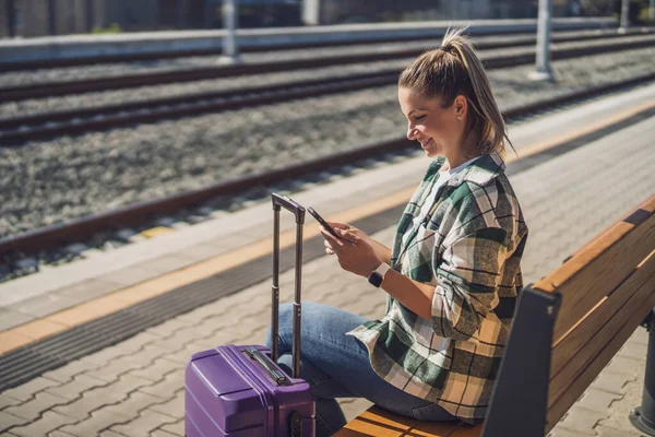 Mulher Feliz Usando Telefone Celular Enquanto Sentado Banco Estação Trem — Fotografia de Stock