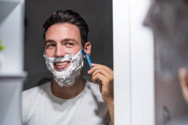 Adam aynada kendine bakarken sakalını tıraş ediyor..