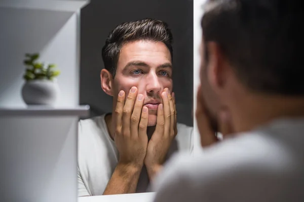 Man looking his eye bags in mirror .