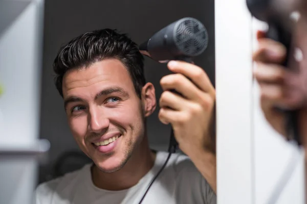 Man using hair dryer while looking himself in the mirror