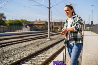 Tren istasyonunda elinde bavulla duran bir kadın saatine bakıyor..
