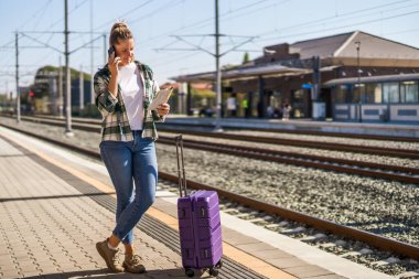 Cep telefonu kullanan ve tren istasyonunda harita tutan mutlu bir kadın..