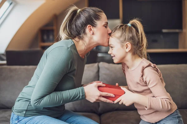 Happy mother is kissing her daughter while  getting gift from her.