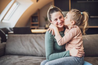 Daughter kissing her happy mother while they spending time home together.