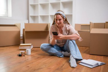 Yeni dairesine taşınırken saçı örgülü, modern kızıl bir kadın telefon kullanıyor..