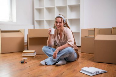 Yeni dairesine taşınırken saçı örgülü, kahve içen modern kızıl bir kadın..