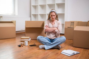 Yeni dairesinde yerde oturan örgülü kızgın kızıl saçlı kadın. Hareket etmekten yoruldu. .