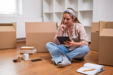 Yeni daireye taşınırken dijital tablet kullanan örgülü modern kızıl kadın..