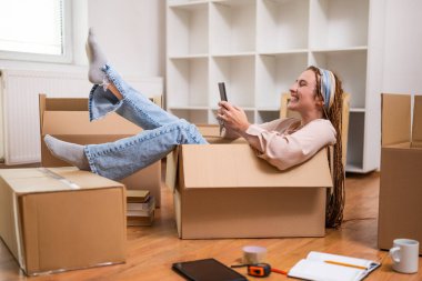 Mutlu kadın telefon kullanıyor ve yeni daireye taşınırken eğleniyor..