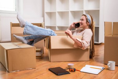 Mutlu kadın telefon kullanıyor ve yeni daireye taşınırken eğleniyor..