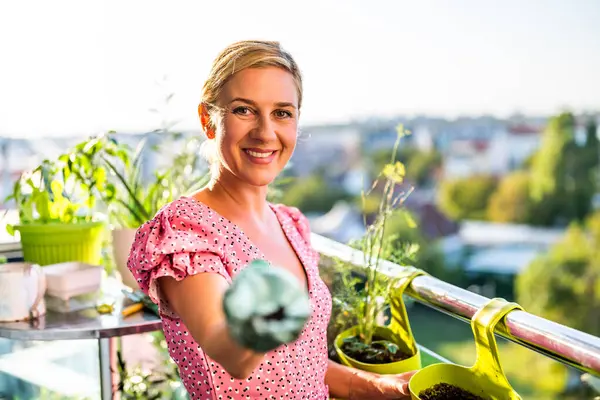 Happy woman enjoys in  gardening on balcony at her home. She is showing soil for her plants.