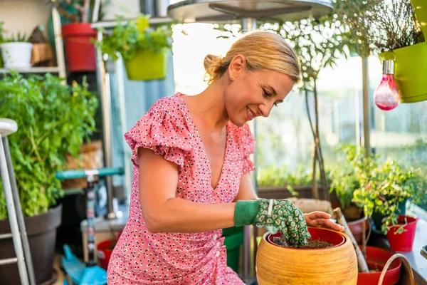 Happy woman enjoys in  gardening on balcony at her home. She is putting soil into flower pot.