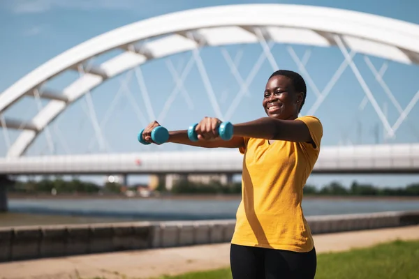 Young woman enjoys  exercising  with weights outdoor.