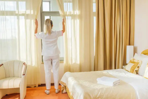 Image of  hotel maid opening window curtains  in a room.