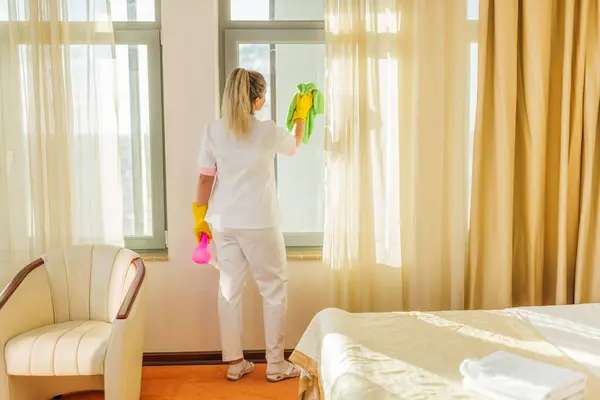 Image of  hotel maid cleaning windows in a room.