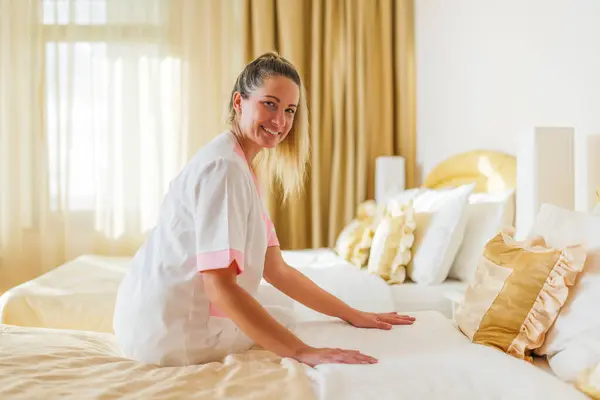 Beautiful hotel maid  making bed in a room.