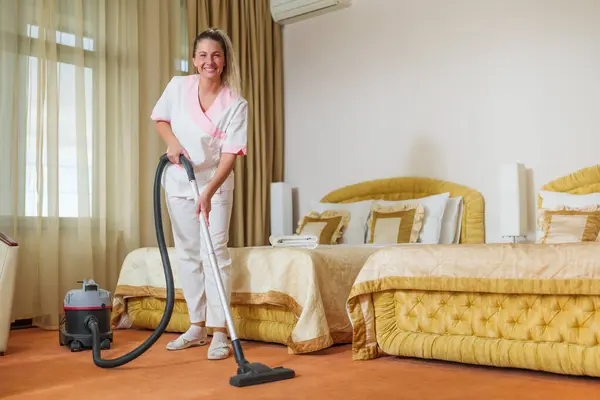 Beautiful hotel maid   vacuuming  room.
