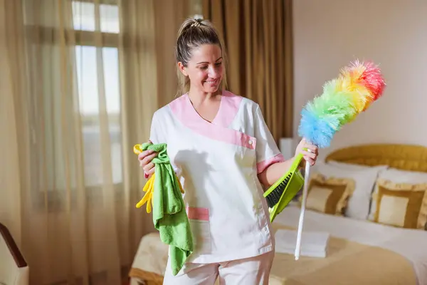 Beautiful hotel maid holding cleaning equipment.
