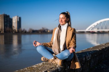 Güzel bir kadın güneşli bir kış gününde nehrin kenarında meditasyon yapmaktan hoşlanır..