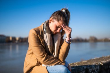 Nehir kenarında otururken baş ağrısı çeken endişeli bir kadın..