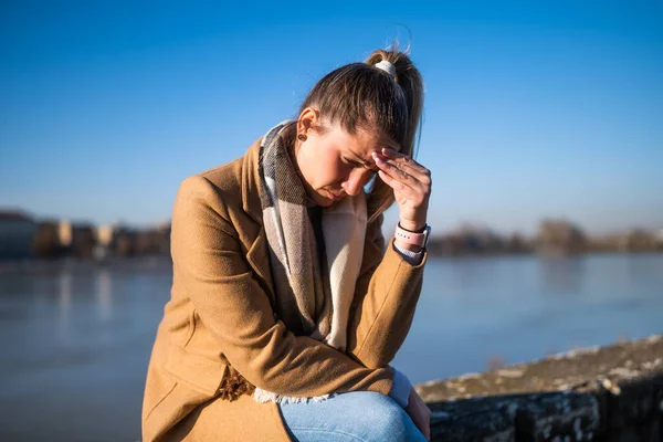 Nehir kenarında otururken baş ağrısı çeken endişeli bir kadın..